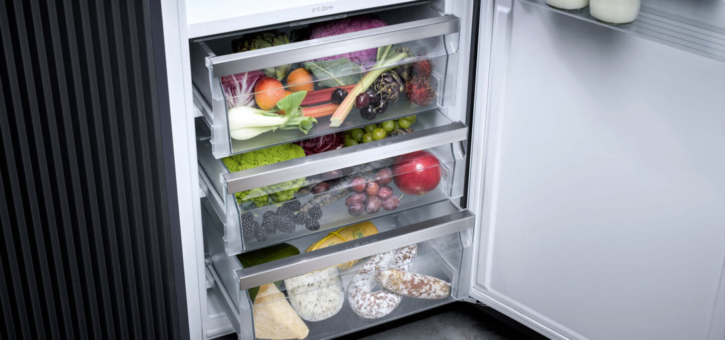 Ein Gemüsefach, ein Obstfach und ein Wurst und Käsefach in einem offenen Kühlschrank von Miele.