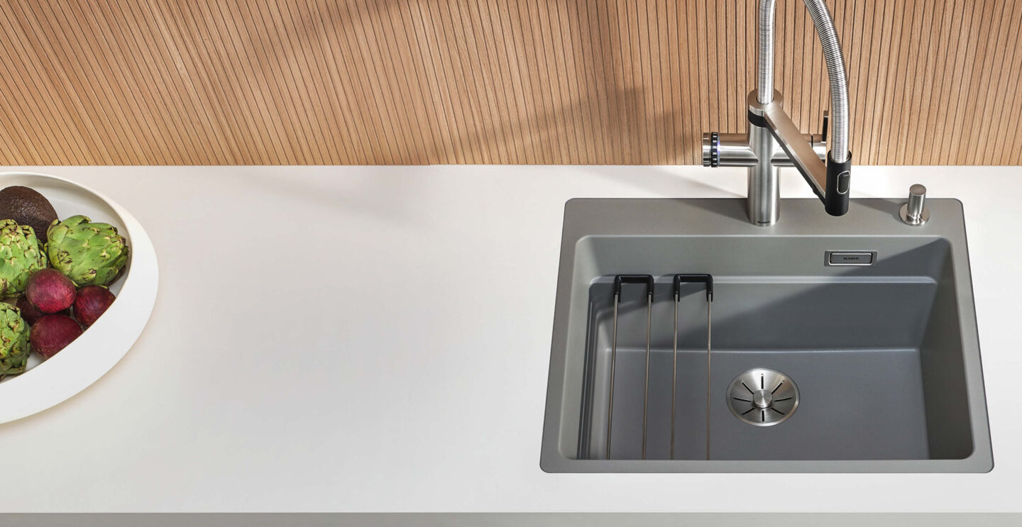 Silgranit Spülbecken von Blanco in Grau ini einer weißen Küchenarbeitsplatte mit Holznischenrückwand.