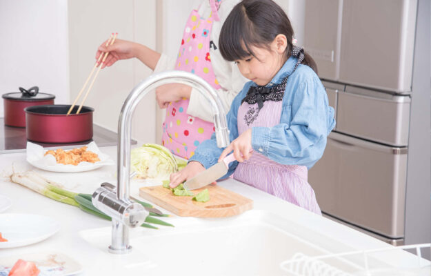 Kleines asiatisches Mädchen schneidet Salat.