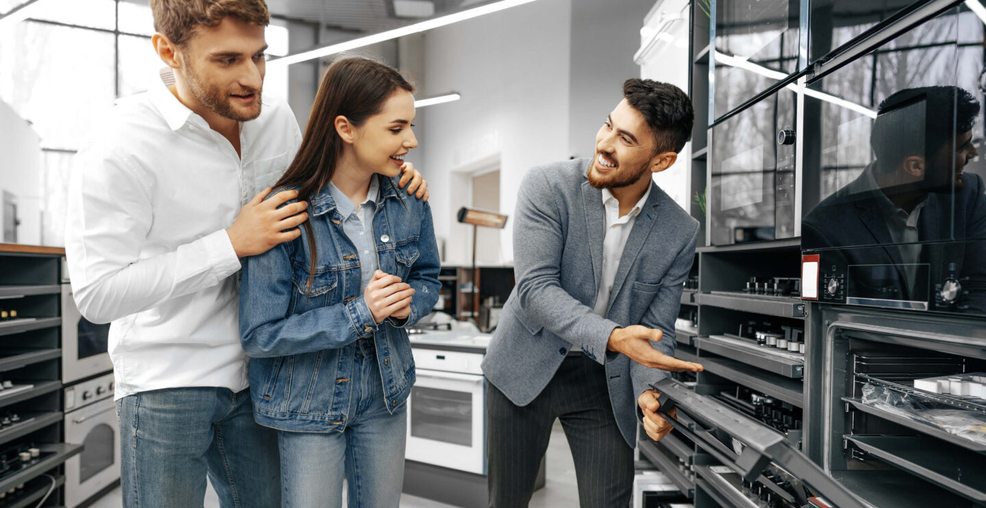 Ein freundlicher Herr berät ein junges Paar zum Thema Kombigeräte in der Küche