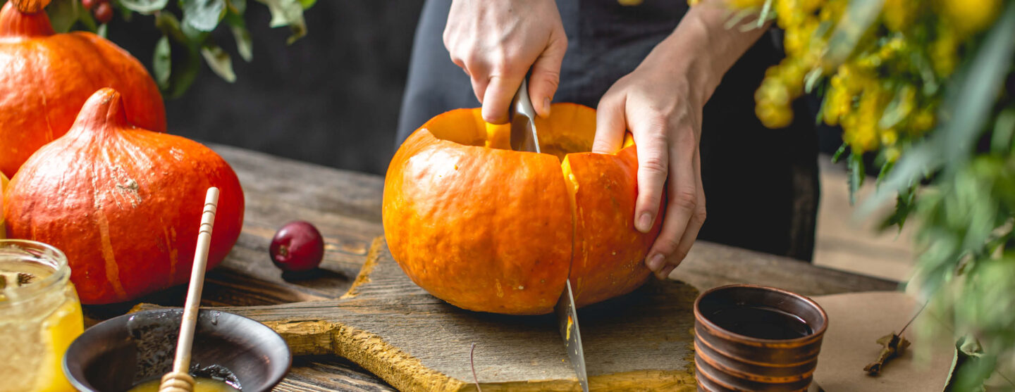 Eine Person halbiert einen Kürbis mit einem großen Messer.