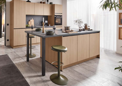 Moderne Küche mit grifflosen Holzfronten, Kochinsel und schwarzer Steinarbeitsplatte von Häcker Küchen.