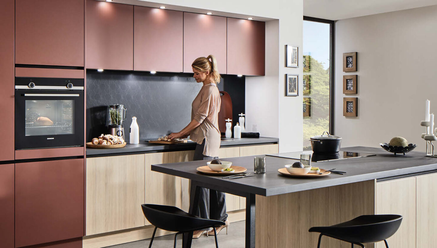 Eine Frau schneidet in einer roten Küche mit Kochinsel und schwarzer Arbeitsplatte Pilze.