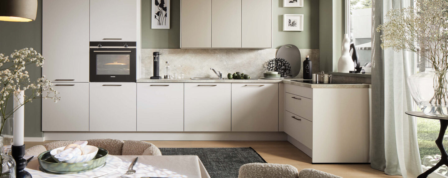 Freundliche Wohnküche mit grün gestrichener Wand, neutralen Fronten und modernem Dekor.