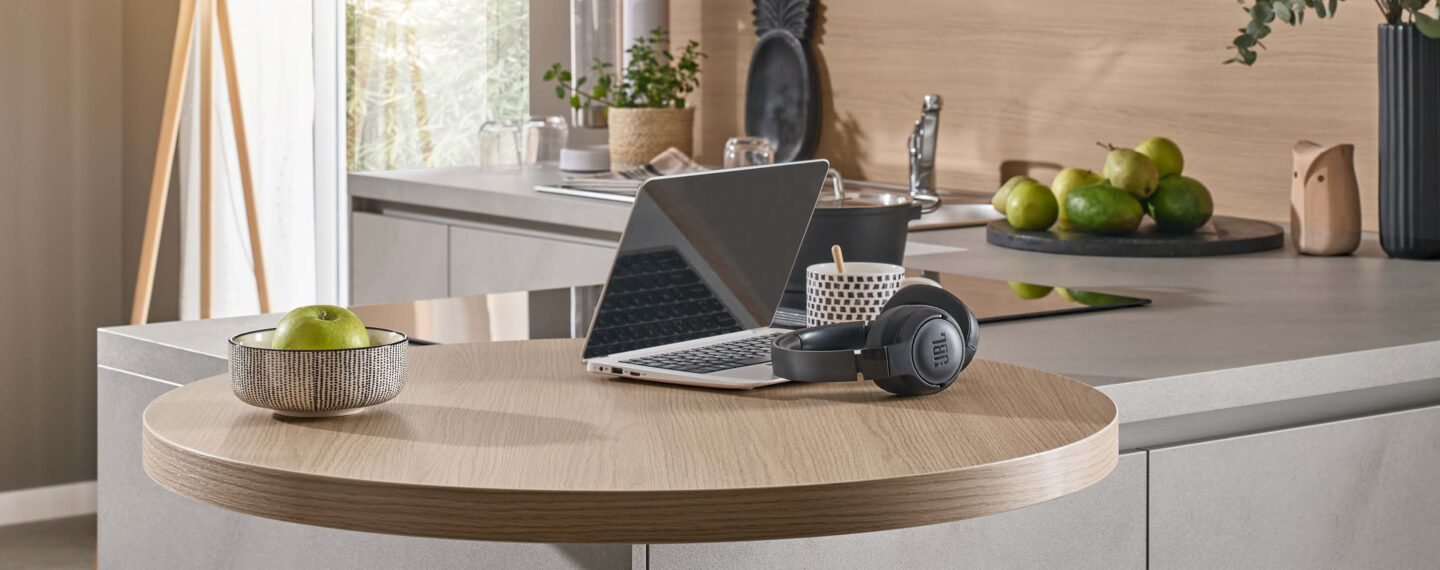 Multifunktionale Küche planen mit runder Ansetztisch-Lösung an der Kücheninsel, genutzt als Arbeitsplatz mit Laptop in moderner Wohnküche.