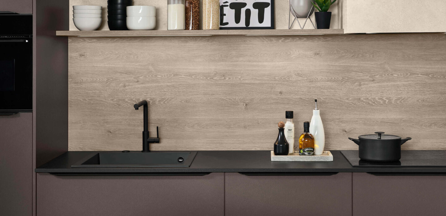 Moderne Nobilia Küche in dunklem Braun mit schwarzer Arbeitsplatte, Spüle und Holzrückwand – hochwertige Einbauküche bei Küchenstyle.