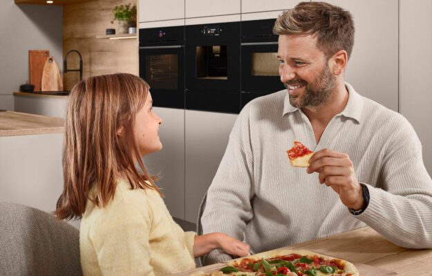 Bild von nobilia: Vater und Tochter sitzen in Küche und essen gemeinsam Pizza