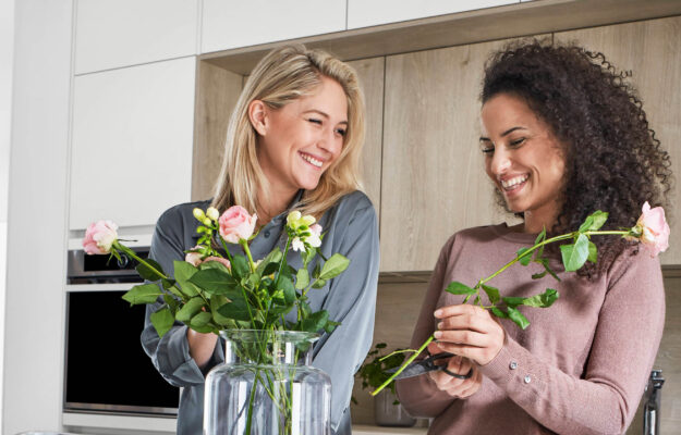 Zwei Freundinnen stehen in Küche von nobilia und befallen eine Glasvase mit Rosen