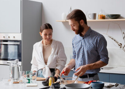 Eine Frau und ein Mann bereiten gemeinsam Essen in einer modernen Küche mit Kücheninsel, großzügiger Arbeitsfläche, Einbauofen und funktionalen Küchenmöbeln zu.
