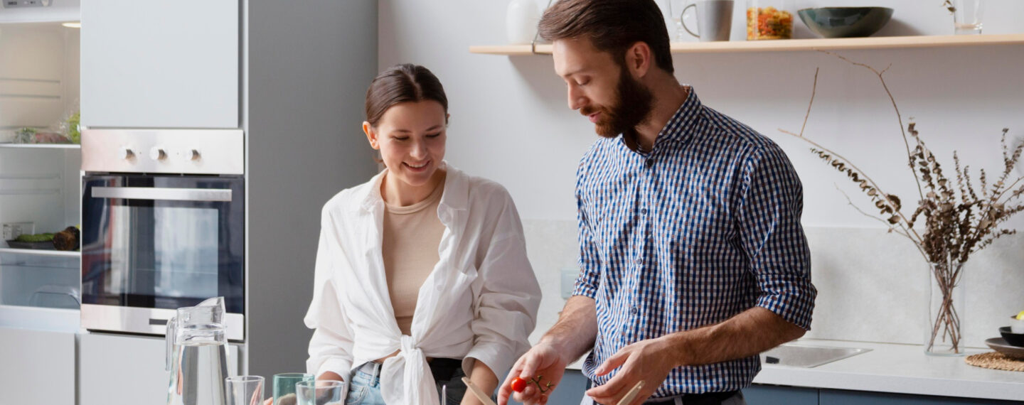 Zwei Personen bereiten gemeinsam Essen in einer modernen Küche mit großzügiger Arbeitsfläche, hellen Küchenmöbeln, Einbauofen und funktionaler Küchenplanung zu.